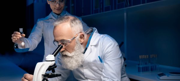 concentrated scientist using microscope while colleague holding