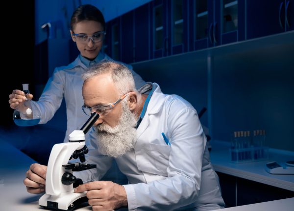 concentrated scientist using microscope while colleague holding