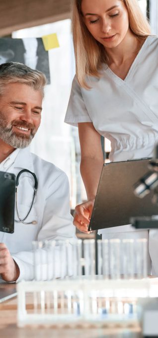 Two clinic workers are indoors together. Senior man with young woman