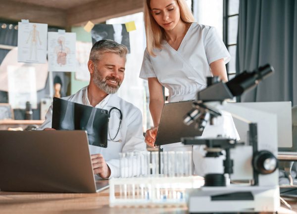 Two clinic workers are indoors together. Senior man with young woman